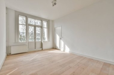 an empty room with wood flooring and large windows in the corners on the left is a white wall