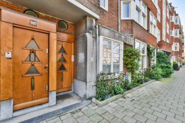 Amsterdam, Netherlands - 10 April, 2021: a bricked building with wooden doors and plants growing on the side of the street in front of the house
