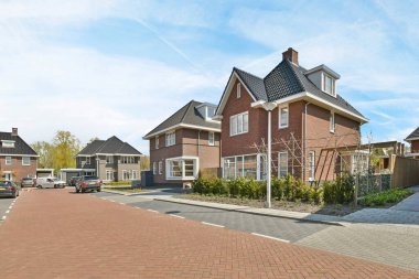 Amsterdam, Netherlands - 10 April, 2021: a street with houses and cars parked on the side, in front of it is a blue sky filled with white clouds