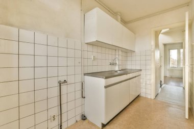 a kitchen with white tiles on the walls and counters in the corner, as seen from the doorway to the right