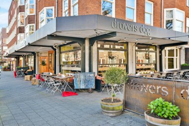 Amsterdam, Netherlands - 10 April, 2021: an outdoor restaurant with tables and chairs on the sidewalk in front of a brick building that has graffiti written on it