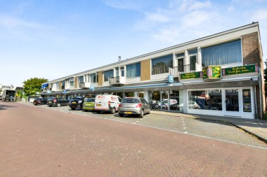 Amsterdam, Netherlands - 10 April, 2021: a city street with cars parked in front of buildings and shops on both sides, the sky is very blue