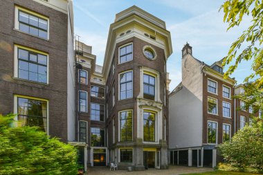 Amsterdam, Netherlands - 10 April, 2021: a building with a clock on its side and some trees in the fore - eye area behind them