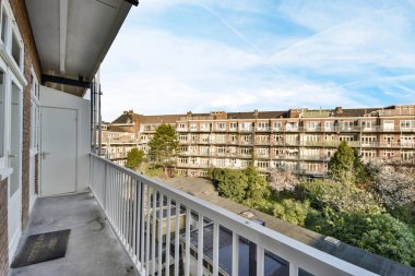 Arka planda ağaçlar ve binalar olan bir balkon, aşağıdaki sokağa bakan bir apartman penceresinden alınmış.