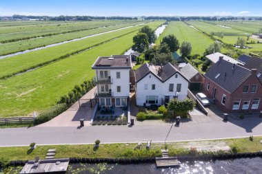 Amsterdam, Netherlands - 10 April, 2021: an aerial view of houses on the river bank in rural area, with green fields and blue sky overhead photo taken from above