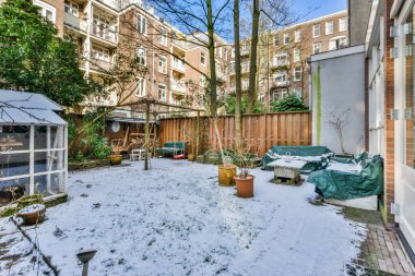a backyard area with snow on the ground and trees in the yard, some buildings are visible to the right