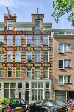 Amsterdam, Netherlands - 10 April, 2021: some cars parked in front of an apartment building with many windows and bales on the side of the street