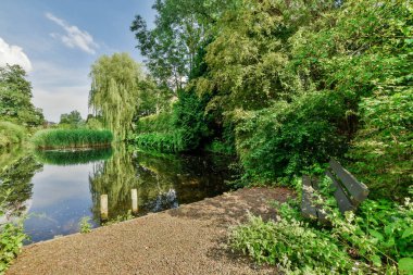 a river in the middle of a park with trees and bushes surrounding it on a bright sunny day stock photo
