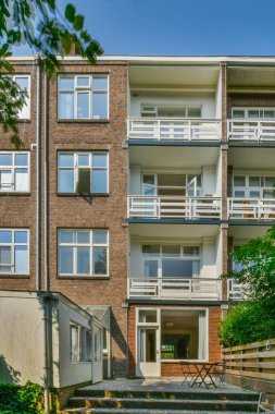an apartment building in the day time with blue sky and green trees on either side, it is very sunny