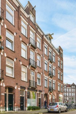 Amsterdam, Netherlands - 10 April, 2021: an apartment building with cars parked on the street next to it and people walking down the sidewalk in front of them