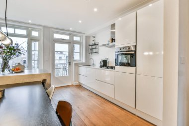 Ahşap döşemeli, beyaz dolaplı ve duvarında fırın olan bir evde mutfak ve yemek odası.