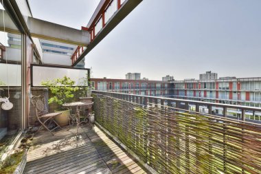 Korkuluklarda birkaç sandalye ve bitki olan bir balkon, kırmızıya boyanmış bir apartmanın önünde.