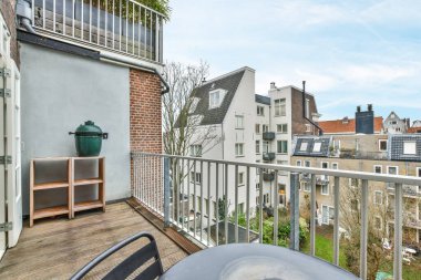 Masasında ızgara olan bir balkon ve verandaya çıkan açık bir kapının önündeki sandalyeler.