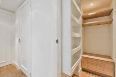 Dolabın içinde ahşap döşemeler ve beyaz dolaplar var. Kapı açık.