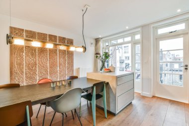 Ahşap döşemeli bir odada yemek masası ve sandalyeler, beyaz duvarlar ve sokağa bakan büyük pencereler.