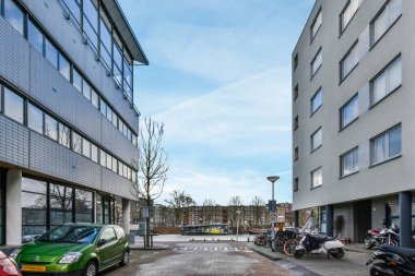 Soldaki binanın önünde park etmiş arabaların ve motosikletlerin olduğu bir cadde boş bir otopark.