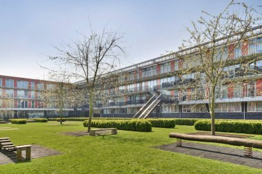 Amsterdam, Hollanda - 10 Nisan 2021: Yeşil çimenlerle çevrili bir apartmanın ortasında ağaçlarla ve banklarla çevrili bir park