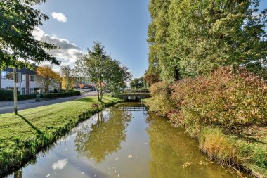 Amsterdam, Hollanda - 10 Nisan 2021: Her iki tarafında evler ve ağaçlar olan bir yerleşim bölgesinin ortasında açık mavi bir gökyüzü var.