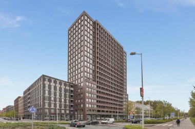 Amsterdam, Hollanda - 10 Nisan 2021: Sokakta arabaları olan ve kaldırımda yürüyen insanların bulunduğu büyük bir bina