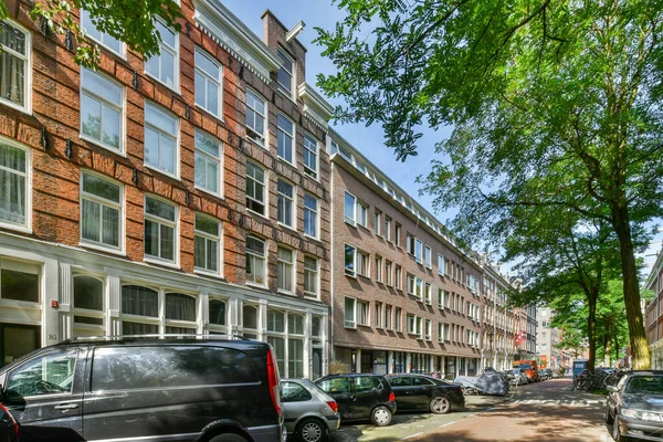 2021年4月10日 荷兰阿姆斯特丹 一些汽车停在街道旁边的一排砖墙公寓楼前 人行道上排列着树木 — 图库照片