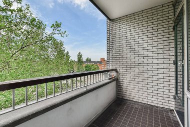 Arka planda ağaçlar ve mavi gökyüzü olan bir balkon, üst kattaki bir apartmandan alındı.