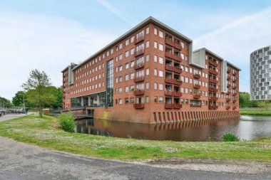 Arka planda binalar ve yerde yeşil çimenler olan bir su kütlesinin yanında bir apartman dairesi.