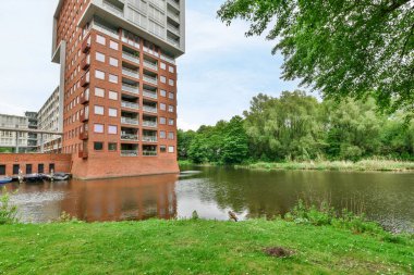 Nehrin önünde tekneler ve etrafında yeşil çimenler olan bir su kütlesinin yanında bir apartman dairesi.