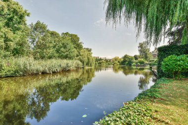 Amsterdam, Hollanda - 10 Nisan 2021: Önünde ağaçlar ve çalılar olan bir nehir, deniz kenarındaki bir tekneden diğer kıyıya götürüldü.