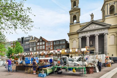 İnsanların alışveriş yaptığı ve kaldırımda eşya sattığı bir açık hava pazarı büyük bir kilise sarp binasının önünde.