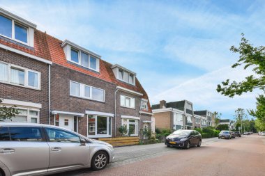 Amsterdam, Hollanda - 10 Nisan 2021: bazı arabalar beyaz pencereli ve kırmızı çatılı tuğlalı evlerin önünde yol kenarına park ettiler