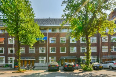 Bir apartman dairesi, yanında arabaları olan bir apartman ve binanın önünde büyüyen iki ağaç.