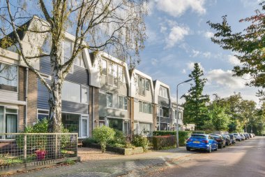 Amsterdam, Hollanda - 10 Nisan 2021: Sokakta arabaların ve ağaçların olduğu bir yerleşim alanı çok mavi bir gökyüzü.