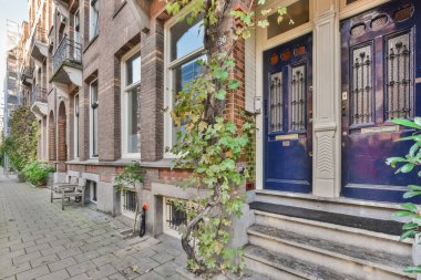 Evin önünde caddenin kenarında büyüyen mavi kapıları ve yeşil sarmaşıkları olan tuğla bir bina.