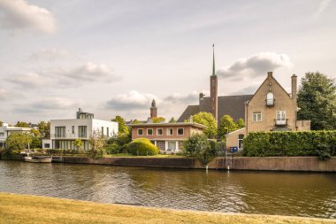 Arka planda binalar ve kenarlarda ağaçlar olan bir su kütlesinin kenarındaki bazı evler.