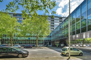 Önünde arabalar olan bir ofis binası ve kaldırımda ağaçlar var.