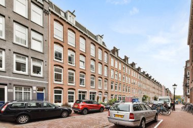 Amsterdam, Netherlands - 10 April, 2021: some cars parked on the side of a street in an urban area with bricked buildings and blue sky above