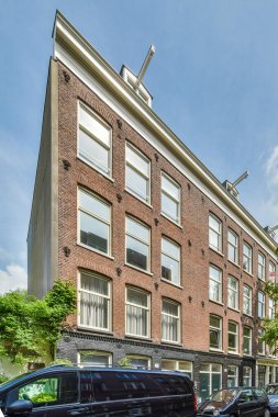 Amsterdam, Hollanda - 10 Nisan 2021: binaların yanında Amerikan bayrağı asılı tuğla bir binanın önüne park edilmiş bazı arabalar