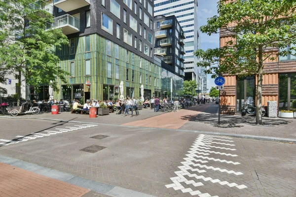 stock image Amsterdam, Netherlands - 10 April, 2021: a building in the middle of an urban area with cars parked on the street and people walking down the sidewalk