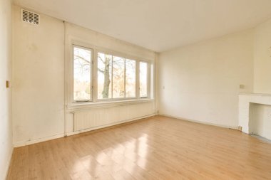 Ahşap döşemeleri ve beyaz duvarları olan boş bir oturma odası. Odada kimse yok.