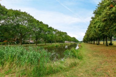 Amsterdam, Hollanda - 10 Nisan 2021: Her iki tarafında ağaçlar ve çimenler olan bir parkın ortasındaki bir nehir.