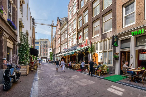 stock image a city street with people sitting at tables and walking on the sidewalk in front of some tall brown brick buildings