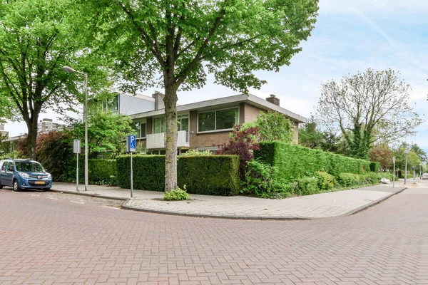 stock image Amsterdam, Netherlands - 10 April, 2021: a street with cars parked on the side and trees lining the road in front of the house thats next door