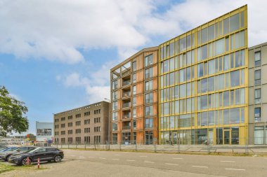 Amsterdam, Hollanda - 10 Nisan 2021: Bir ofis binasının önünde park yeri ve yanında arabaların park yeri ve bulutlarla dolu mavi bir gökyüzü.