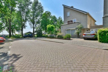 Amsterdam, Hollanda - 10 Nisan 2021: yan tarafında arabalar ve arka tarafında evler olan bir cadde, sağa doğru yol boyunca uzanan ağaçlar