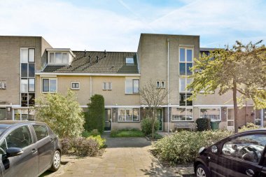 Amsterdam, Hollanda - 10 Nisan 2021: Garaj yolunda arabaları ve sokağın her iki tarafında ağaçları olan bir apartman kompleksi