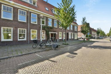 Amsterdam, Netherlands - 10 April, 2021: a brick building on the side of a street with cars parked in front and trees lining the sidewalk behind it