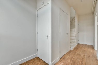 Beyaz duvarları ve sağında ahşap döşemeleri olan boş bir oda. Başka bir odaya açılan bir kapı var.