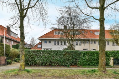 Amsterdam, Hollanda - 10 Nisan 2021: Bahçesinde ağaçlar olan bir ev ve sokağın karşısından görüldüğü üzere evin yanında büyüyen çalılar.