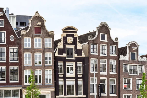 stock image Amsterdam, Netherlands - 10 April, 2021: some very old buildings in the middle of an urban area with blue sky and white clouds above them, on a sunny day