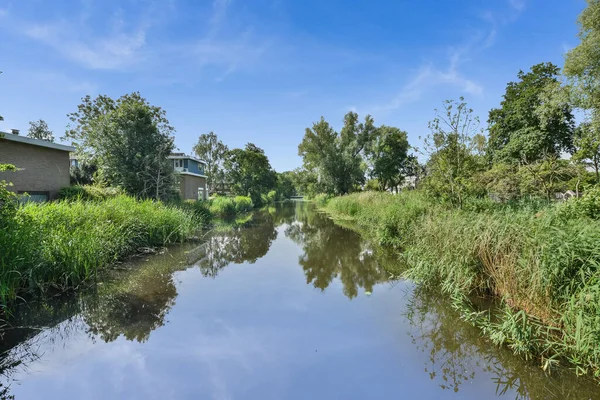 a river with houses in the background and trees on either side, as seen from the waters edge